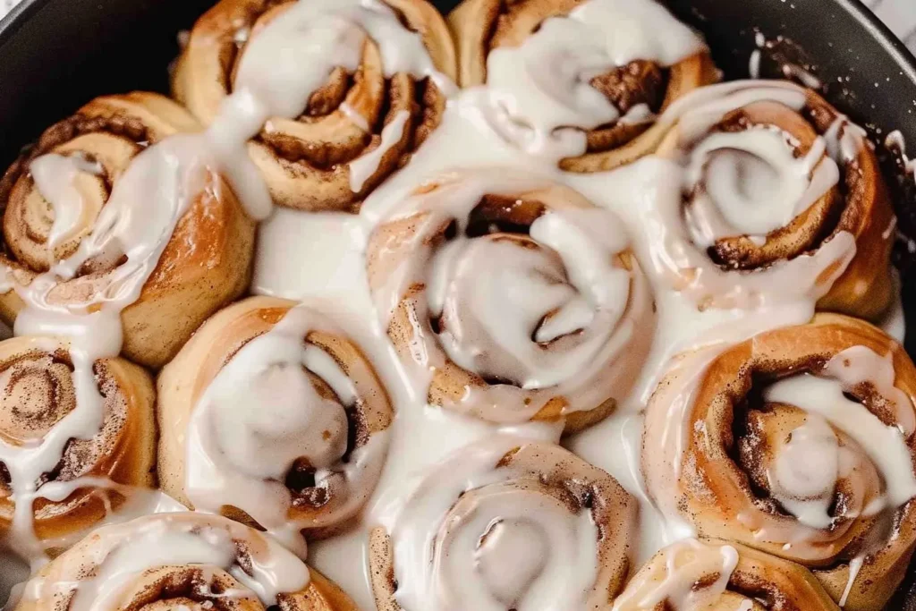 Close-up of freshly baked sourdough cinnamon rolls topped with creamy icing, highlighting their golden-brown texture and swirled cinnamon filling